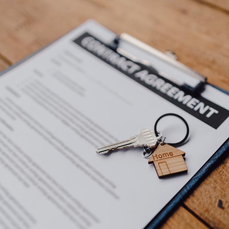Close-up of a tenancy agreement document with a small house keychain on a wooden table, symbolizing real estate or rental property contract.
